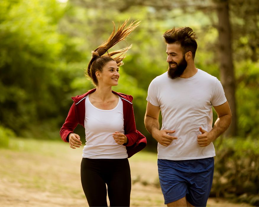 A man and woman jog along a wooded trail together, enjoying active outdoor movement that reflects healthy breathing.
