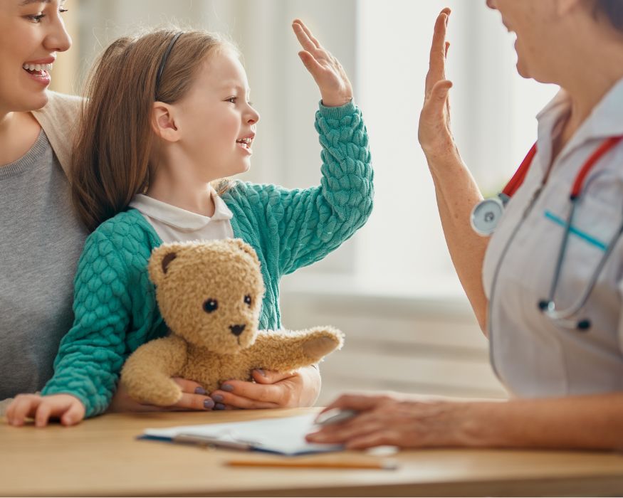 A child holding a teddy bear reaches for a high‑five with a clinician, creating a warm, reassuring moment during a visit.