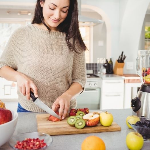 A woman slices fresh fruits and vegetables on a kitchen counter, highlighting nutrient-rich choices that support immune wellness.