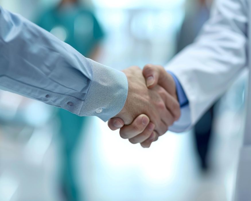A patient and clinician shake hands in a bright medical hallway, reflecting a welcoming start to the visit experience.