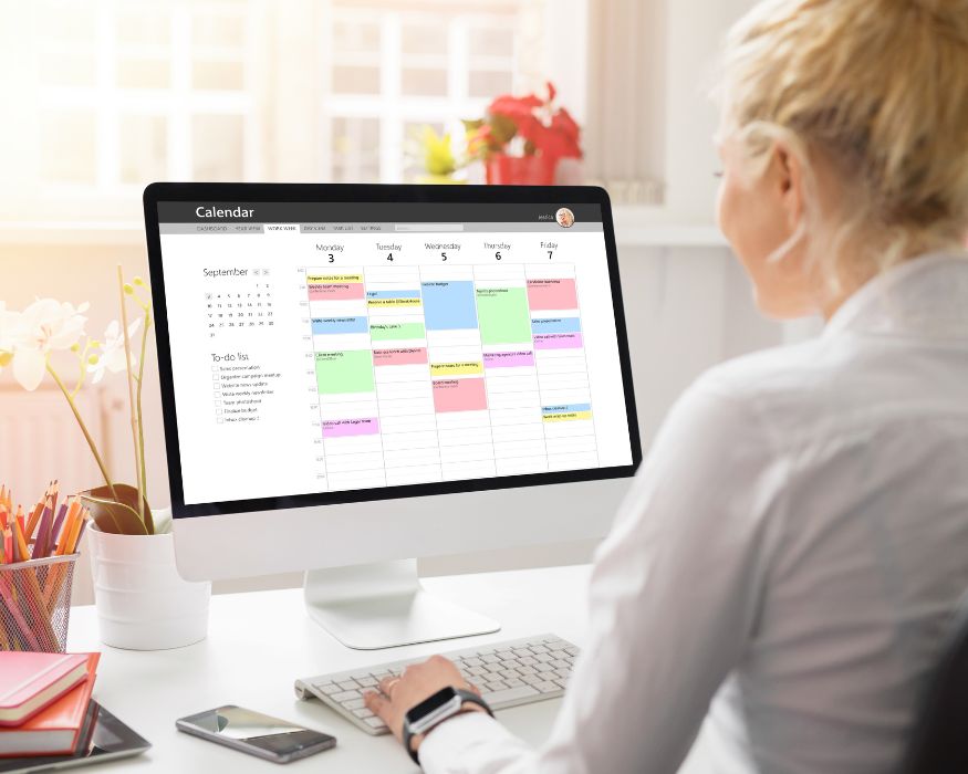 A woman views a colorful weekly calendar on her computer, suggesting easy online scheduling for upcoming appointments.