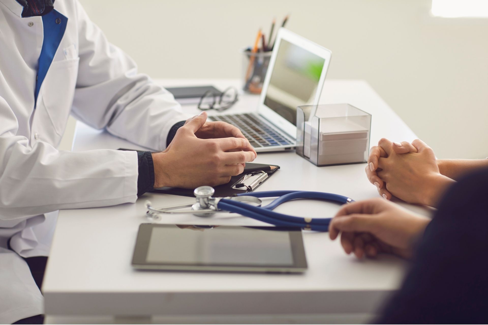 A clinician rests a hand on a patient’s shoulder during a conversation, showing supportive guidance in a calm clinical setting.
