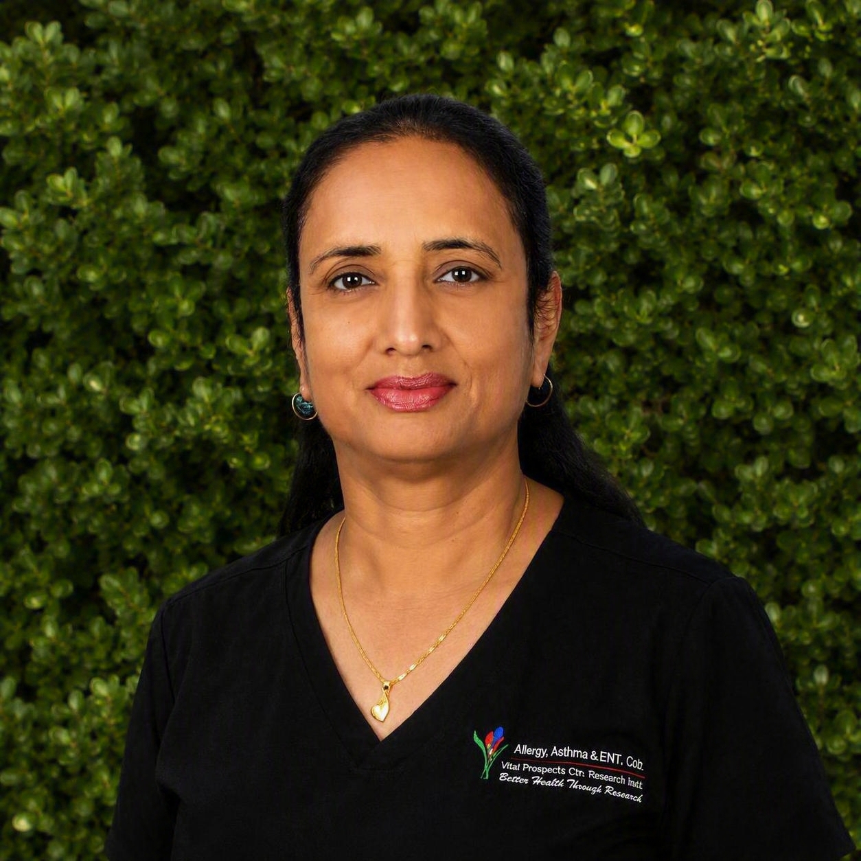A team member in a black AAIC scrub top stands outdoors among green foliage, reflecting dedication to research within the clinic.